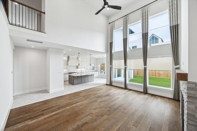 unfurnished living room with light wood-type flooring, a towering ceiling, ceiling fan, and a healthy amount of sunlight