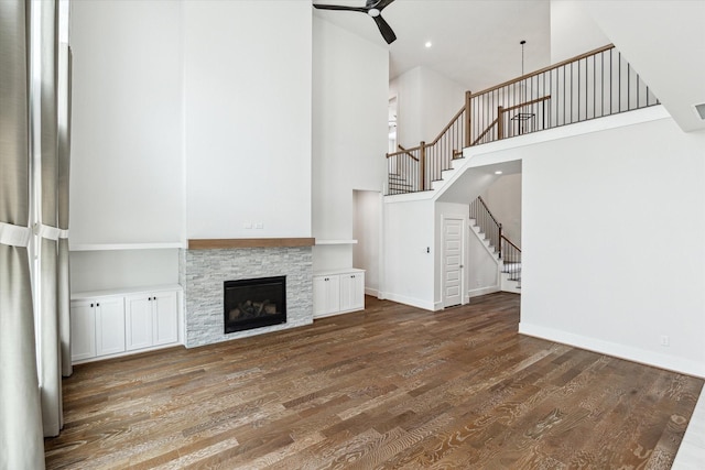 unfurnished living room featuring stairway, a high ceiling, wood finished floors, baseboards, and ceiling fan