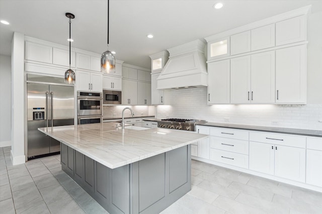 kitchen featuring white cabinets, a sink, custom exhaust hood, backsplash, and built in appliances