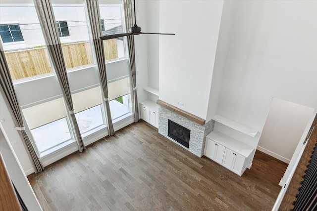unfurnished living room featuring a ceiling fan, wood finished floors, and a stone fireplace