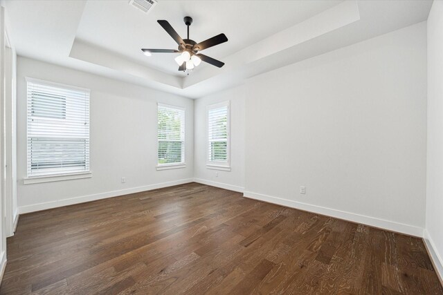 unfurnished room featuring visible vents, baseboards, a tray ceiling, and dark wood finished floors