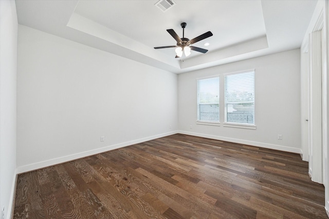 spare room with dark wood-style floors, a raised ceiling, visible vents, a ceiling fan, and baseboards