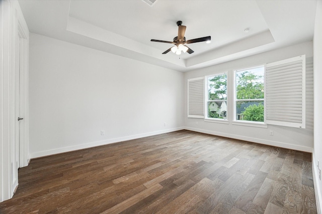 empty room featuring a tray ceiling, baseboards, a ceiling fan, and dark wood-style floors