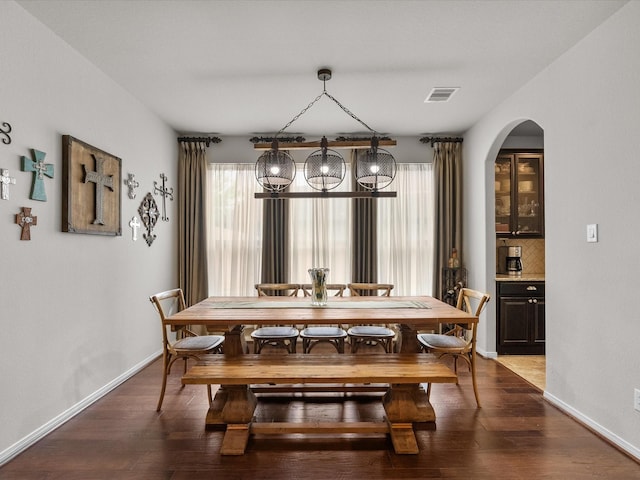 dining area with a wealth of natural light, visible vents, arched walkways, and dark wood-style floors