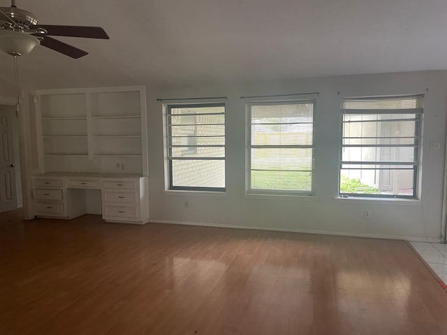 unfurnished living room with a ceiling fan, baseboards, light wood-style flooring, and built in desk