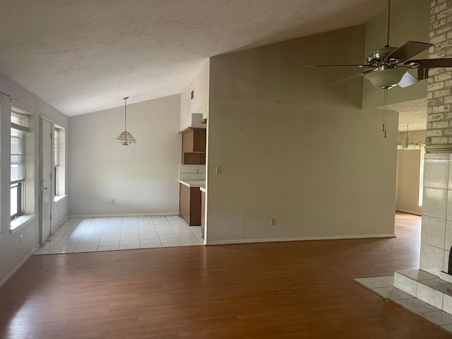 unfurnished living room with a ceiling fan, light wood finished floors, vaulted ceiling, and a textured ceiling