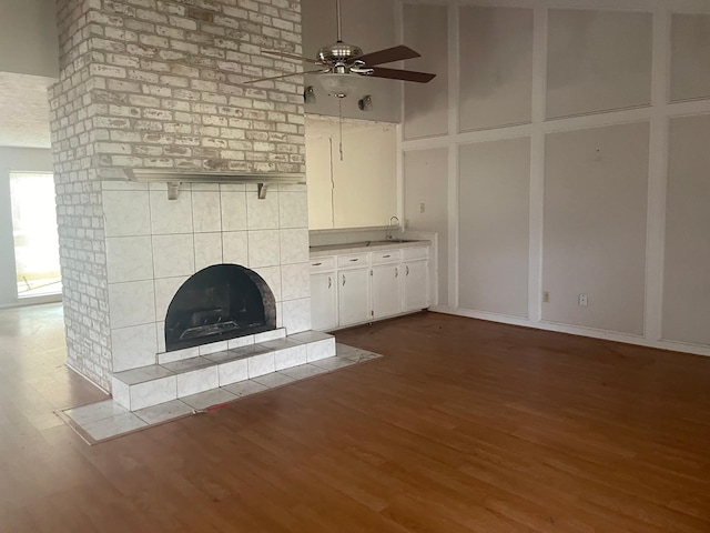 unfurnished living room featuring a fireplace, wood finished floors, a sink, and a ceiling fan