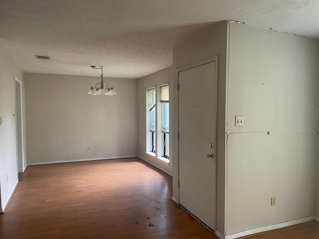 interior space featuring a textured ceiling, visible vents, baseboards, wood finished floors, and a notable chandelier