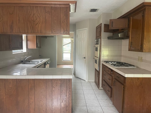 kitchen featuring stainless steel appliances, under cabinet range hood, a sink, visible vents, and a peninsula