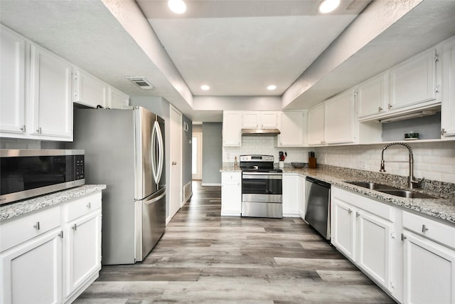kitchen featuring visible vents, stainless steel appliances, a sink, under cabinet range hood, and white cabinetry
