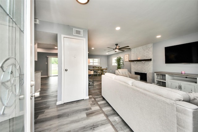 living room featuring ceiling fan, visible vents, a brick fireplace, wood finished floors, and recessed lighting