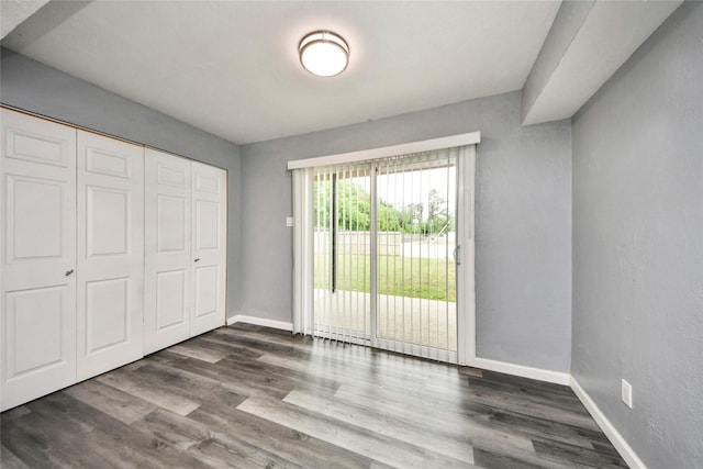 unfurnished bedroom featuring access to outside, baseboards, dark wood-type flooring, and a closet