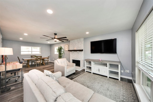 living room featuring a brick fireplace, a ceiling fan, recessed lighting, and dark wood-type flooring
