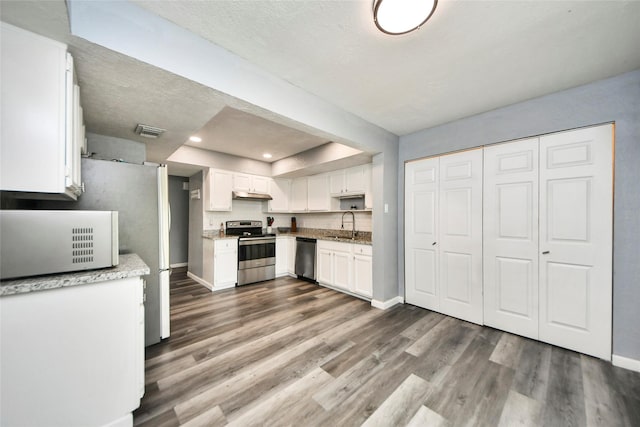 kitchen featuring visible vents, wood finished floors, baseboards, white cabinets, and appliances with stainless steel finishes