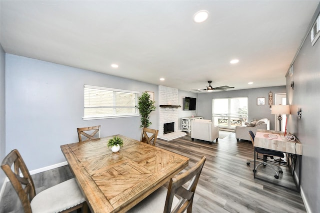 dining space featuring a ceiling fan, a brick fireplace, recessed lighting, and wood finished floors