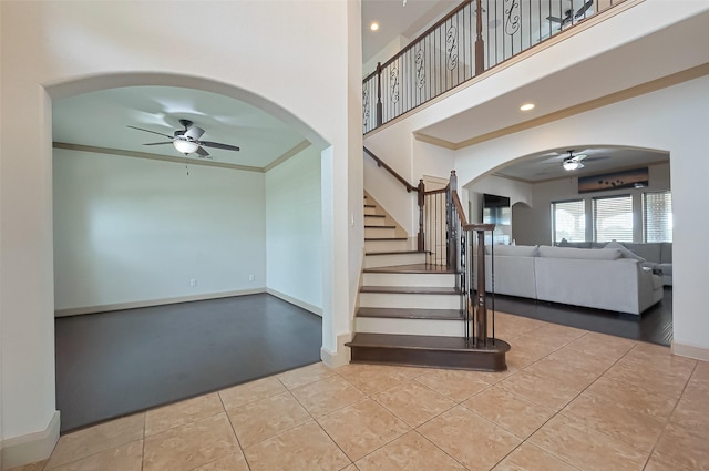 stairway with ornamental molding, baseboards, a towering ceiling, arched walkways, and a ceiling fan