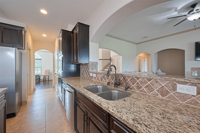 kitchen with tasteful backsplash, stainless steel appliances, a sink, light stone counters, and ceiling fan