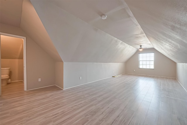 additional living space with light wood-type flooring, ceiling fan, lofted ceiling, and a textured ceiling