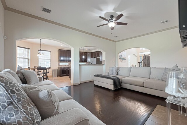 living area featuring arched walkways, visible vents, ceiling fan with notable chandelier, and wood finished floors