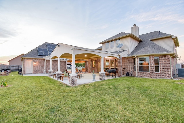 rear view of house with brick siding, solar panels, a yard, and a patio