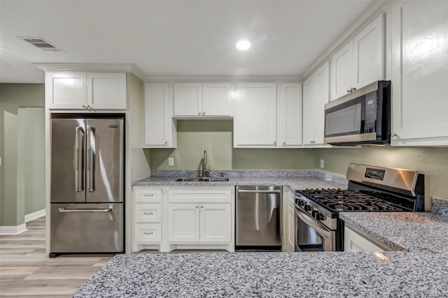 kitchen with white cabinets, visible vents, light stone countertops, appliances with stainless steel finishes, and a sink