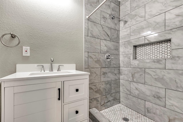 full bathroom with tiled shower, vanity, and a textured wall