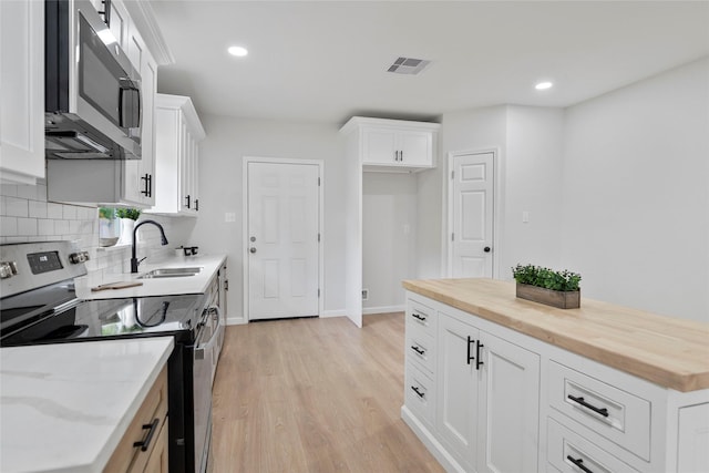 kitchen with light wood-type flooring, wooden counters, stainless steel appliances, and a sink