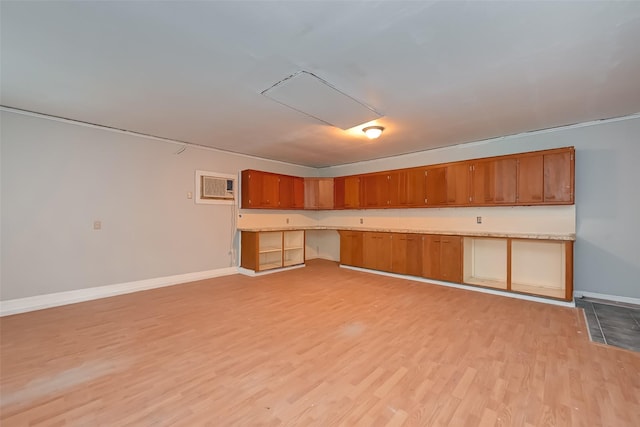 kitchen with brown cabinetry, light countertops, a wall mounted air conditioner, baseboards, and light wood-type flooring