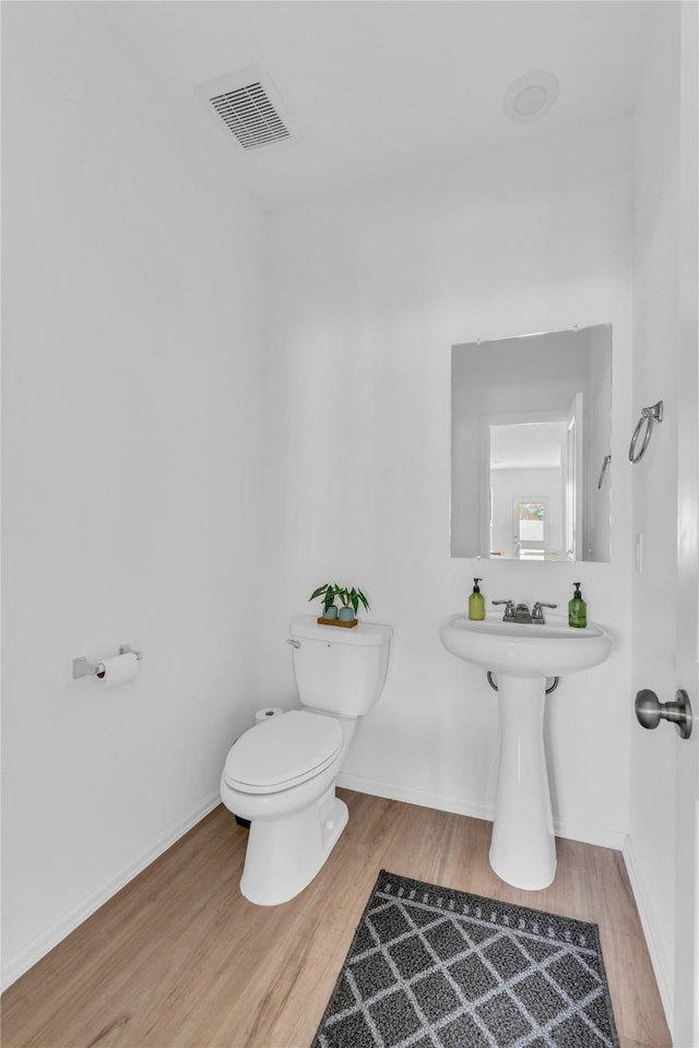 half bathroom with baseboards, wood finished floors, visible vents, and toilet