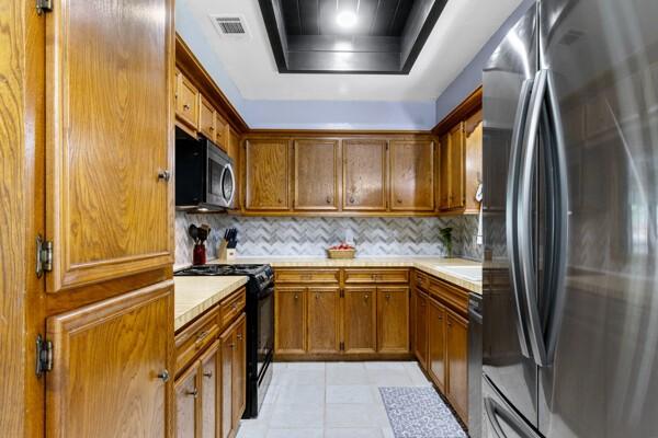 1760 County Road 965, Alvin, TX 77511 - kitchen featuring appliances with stainless steel finishes, light countertops, a tray ceiling, and brown cabinetry
