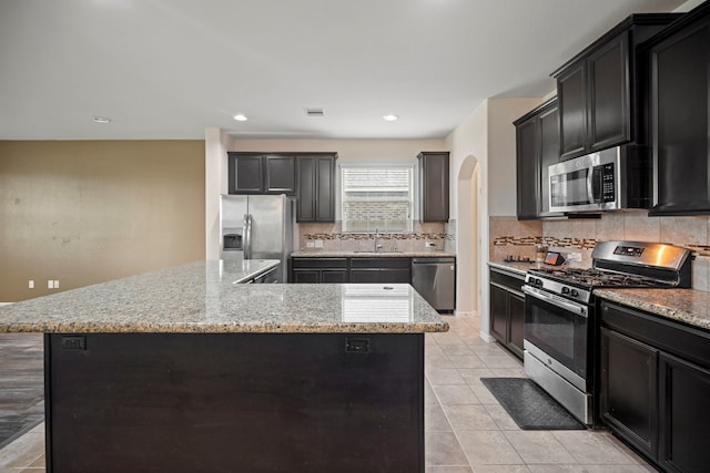 2311 Leonetti Ln, Rosenberg, TX 77471 - kitchen featuring stainless steel appliances, a sink, arched walkways, tasteful backsplash, and a kitchen island
