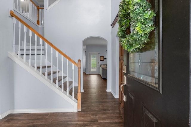 entrance foyer featuring arched walkways, stairs, baseboards, and dark wood finished floors