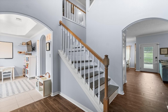 staircase featuring visible vents, crown molding, baseboards, wood finished floors, and arched walkways