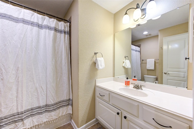 bathroom featuring vanity, baseboards, a textured wall, toilet, and visible vents