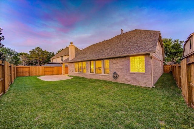 rear view of property with a lawn, roof with shingles, a patio, brick siding, and a chimney