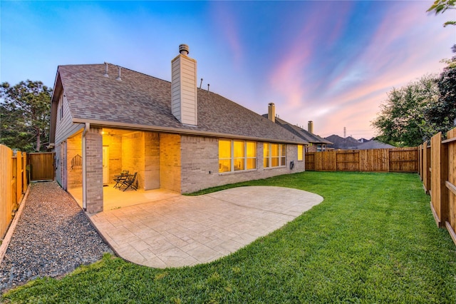 back of property at dusk featuring a patio, brick siding, a yard, and a chimney
