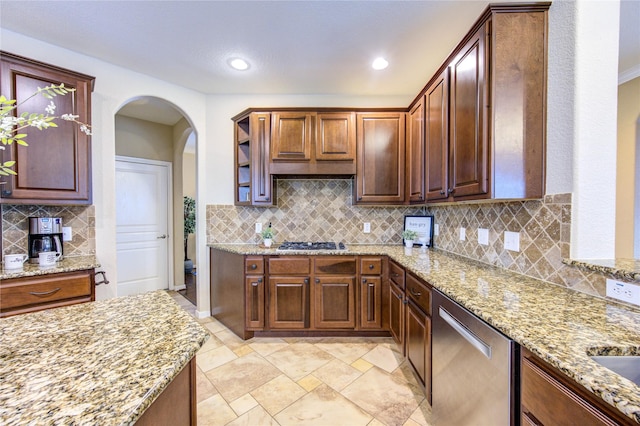 kitchen featuring backsplash, light stone countertops, arched walkways, and stainless steel appliances