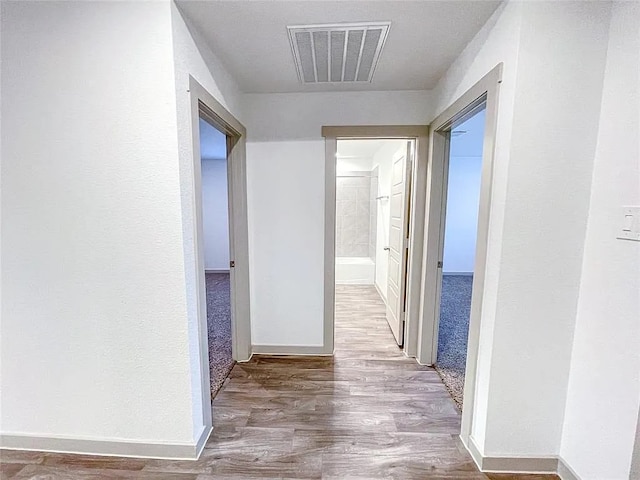 hallway featuring baseboards, visible vents, and wood finished floors
