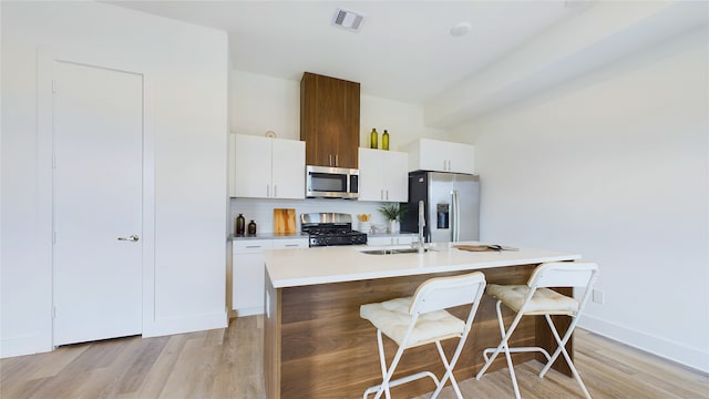 9616 Habitat St, Houston, TX 77075 - kitchen featuring a breakfast bar, a center island with sink, light wood-style flooring, appliances with stainless steel finishes, and visible vents