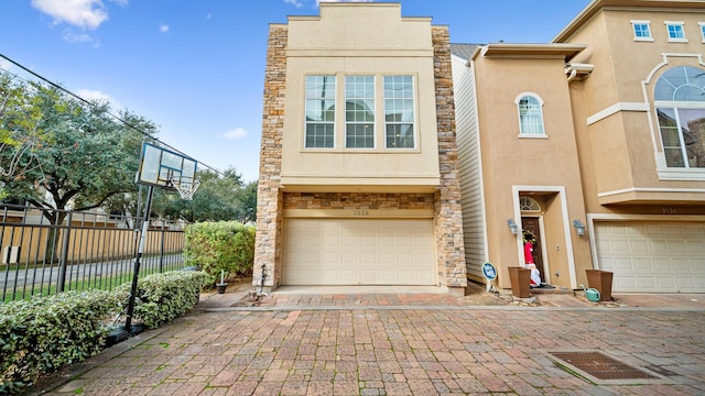 view of front of property with stone siding, fence, decorative driveway, an attached garage, and stucco siding
