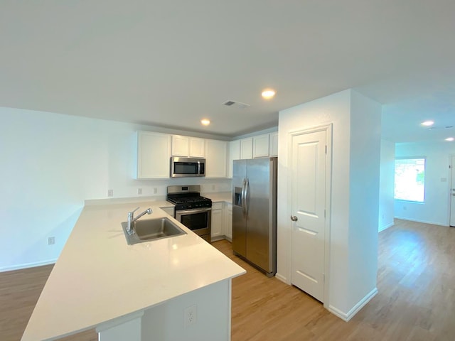 21015 Longeni Dr, New Caney, TX 77357 - kitchen with appliances with stainless steel finishes, a sink, a peninsula, light wood-style floors, and white cabinets