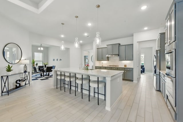 250 Peninsula Point Dr, Montgomery, TX 77356 - kitchen featuring appliances with stainless steel finishes, a kitchen bar, tasteful backsplash, a center island with sink, and light wood-style flooring