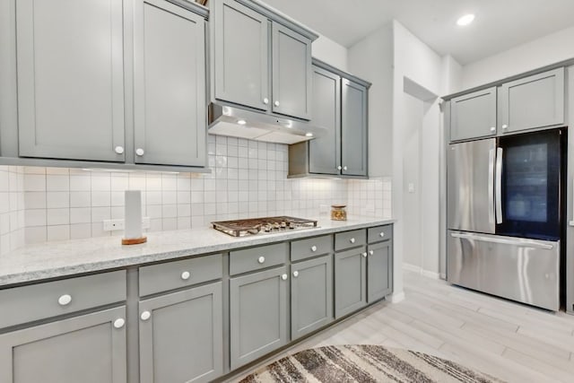250 Peninsula Point Dr, Montgomery, TX 77356 - kitchen featuring appliances with stainless steel finishes, gray cabinets, under cabinet range hood, decorative backsplash, and light stone counters