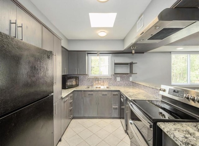 kitchen with light tile patterned floors, exhaust hood, a sink, black appliances, and a skylight