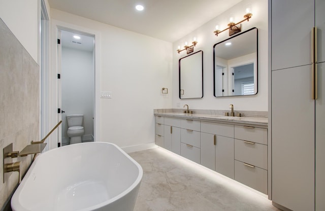 bathroom with double vanity, a freestanding tub, baseboards, recessed lighting, and a sink