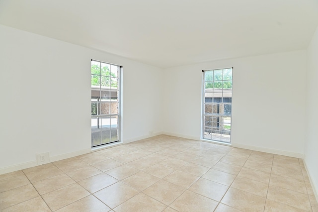 spare room featuring light tile patterned flooring, a wealth of natural light, and baseboards