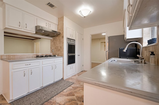 kitchen featuring a sink, under cabinet range hood, decorative backsplash, multiple ovens, and white cabinetry