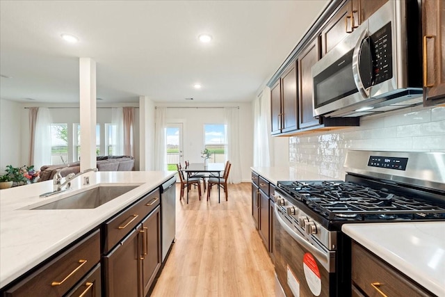 kitchen featuring decorative backsplash, light wood-style flooring, appliances with stainless steel finishes, a sink, and a wealth of natural light