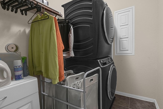 laundry area with dark tile patterned flooring, baseboards, stacked washer and clothes dryer, and laundry area