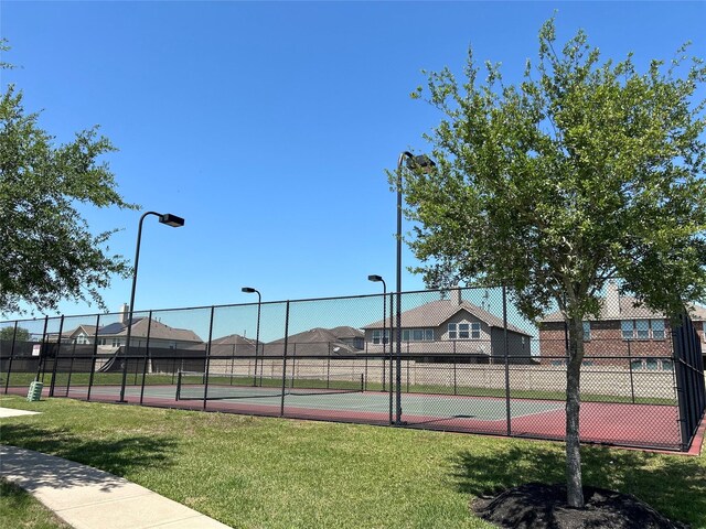view of tennis court featuring fence and a lawn